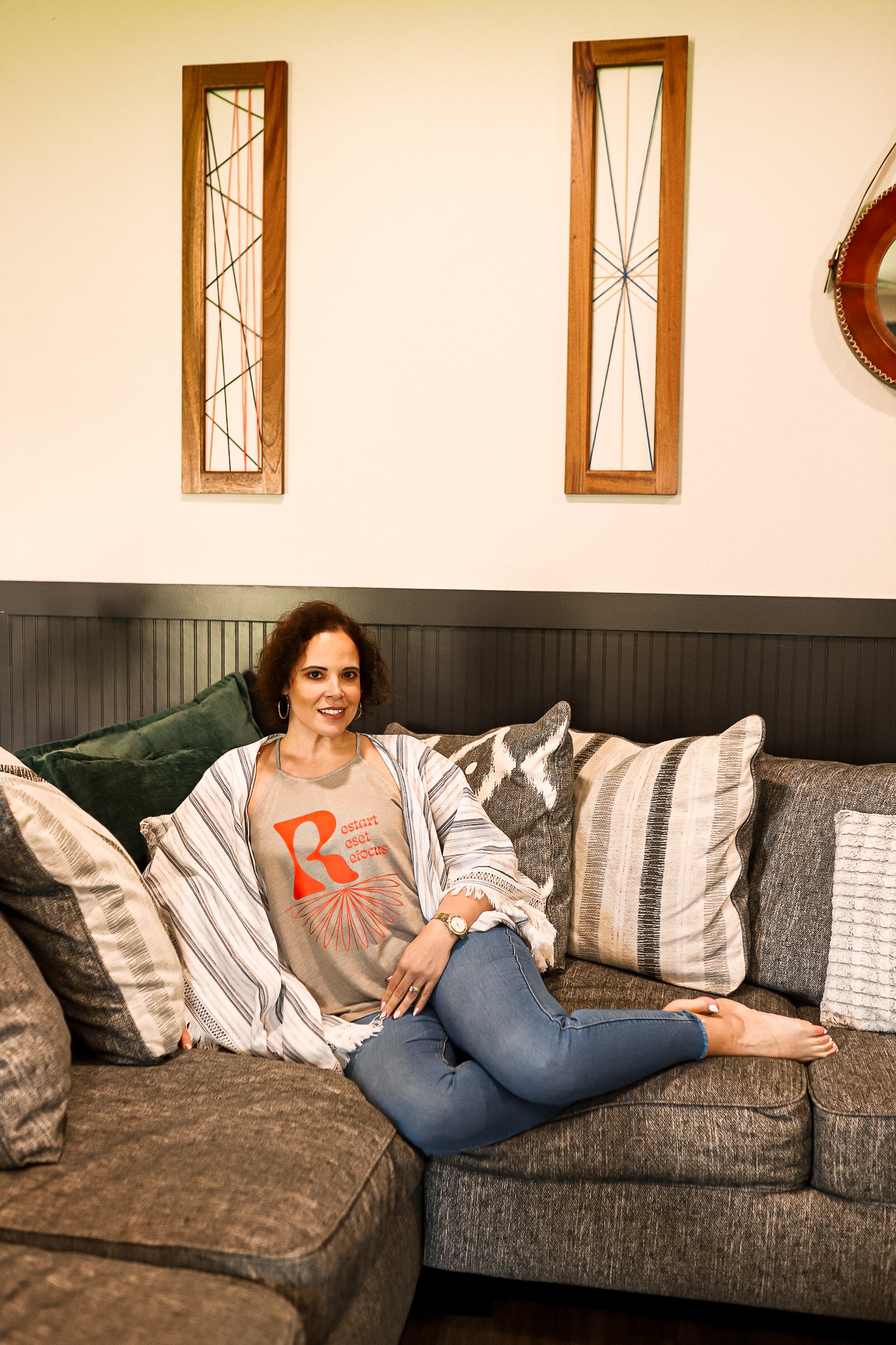 Model Wearing jeans with green/grey slouchy tank laying down on the couch. 