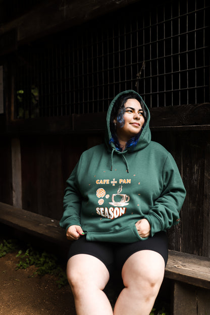 Woman sitting down wearing our " Cafe Con Pan Season" Hoodie in Blueberry color 