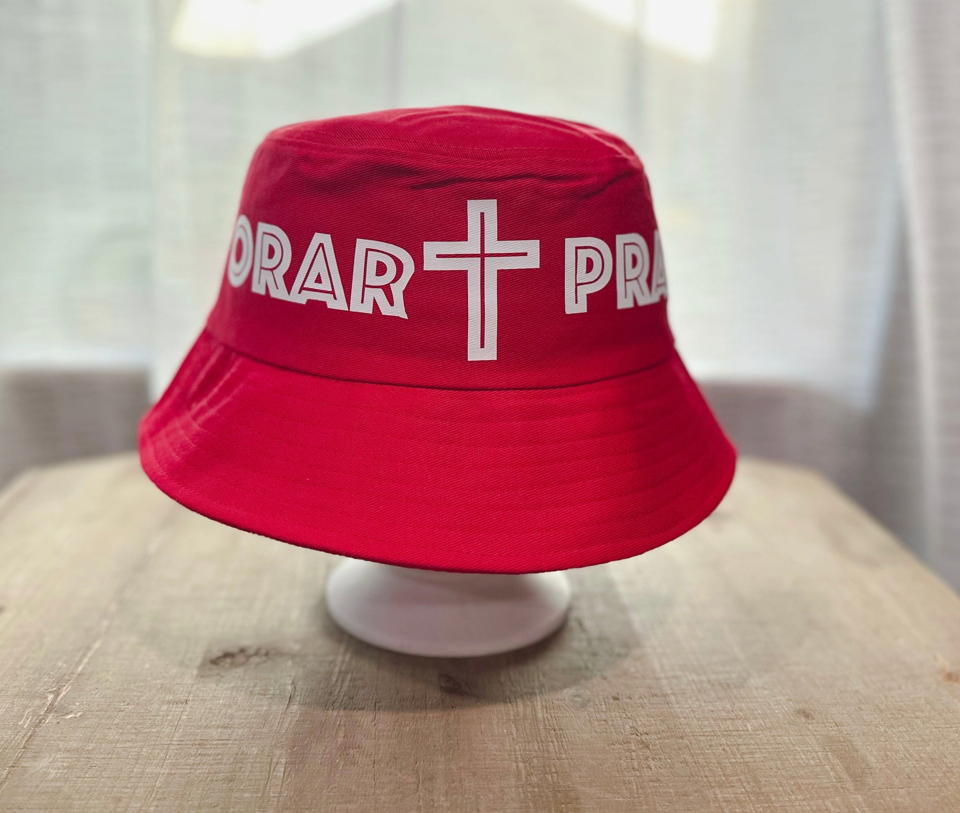 Red Bucket Hat With White Text Saying "Orar Pray" with White Cross In Between. 