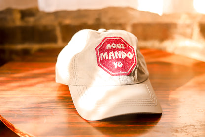 Light grey hat with glitter design saying "Aqui mando yo"