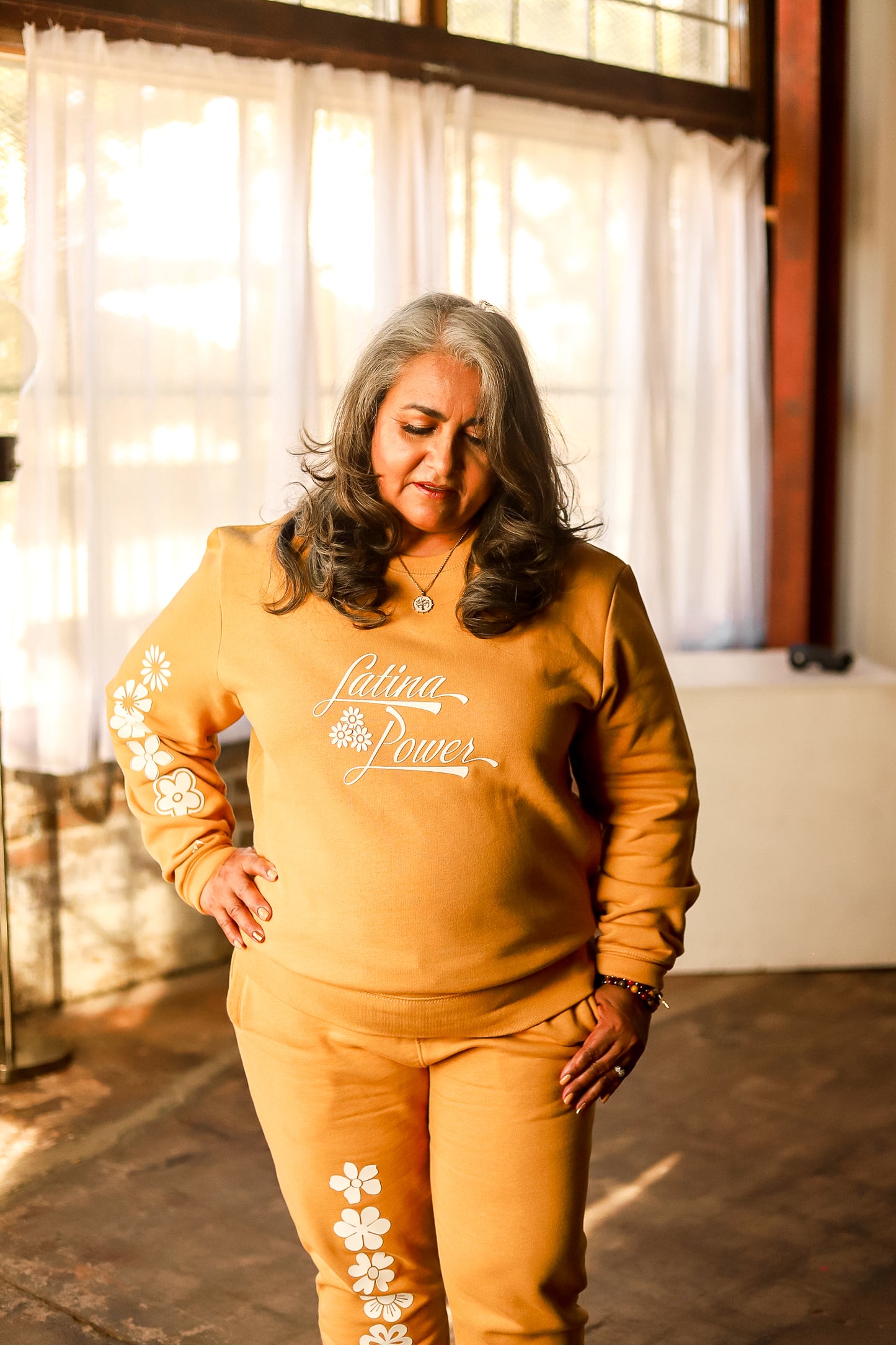 Person wearing a yellow crewneck with white flowers and "Latina Power' saying and yellow joggers with white flower design. 